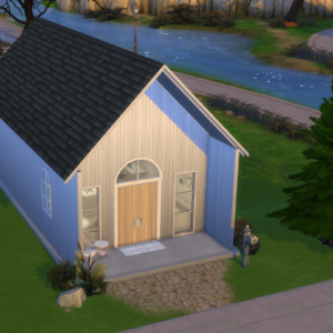 A compact, contemporary blue house measuring 20x35 ft features a black roof and a spacious wooden front door, perfectly situated near a tranquil river. The landscaped yard includes shrubs and a towering tree, with a cobblestone path leading to the entrance of this chic Alix Tiny House Kit.